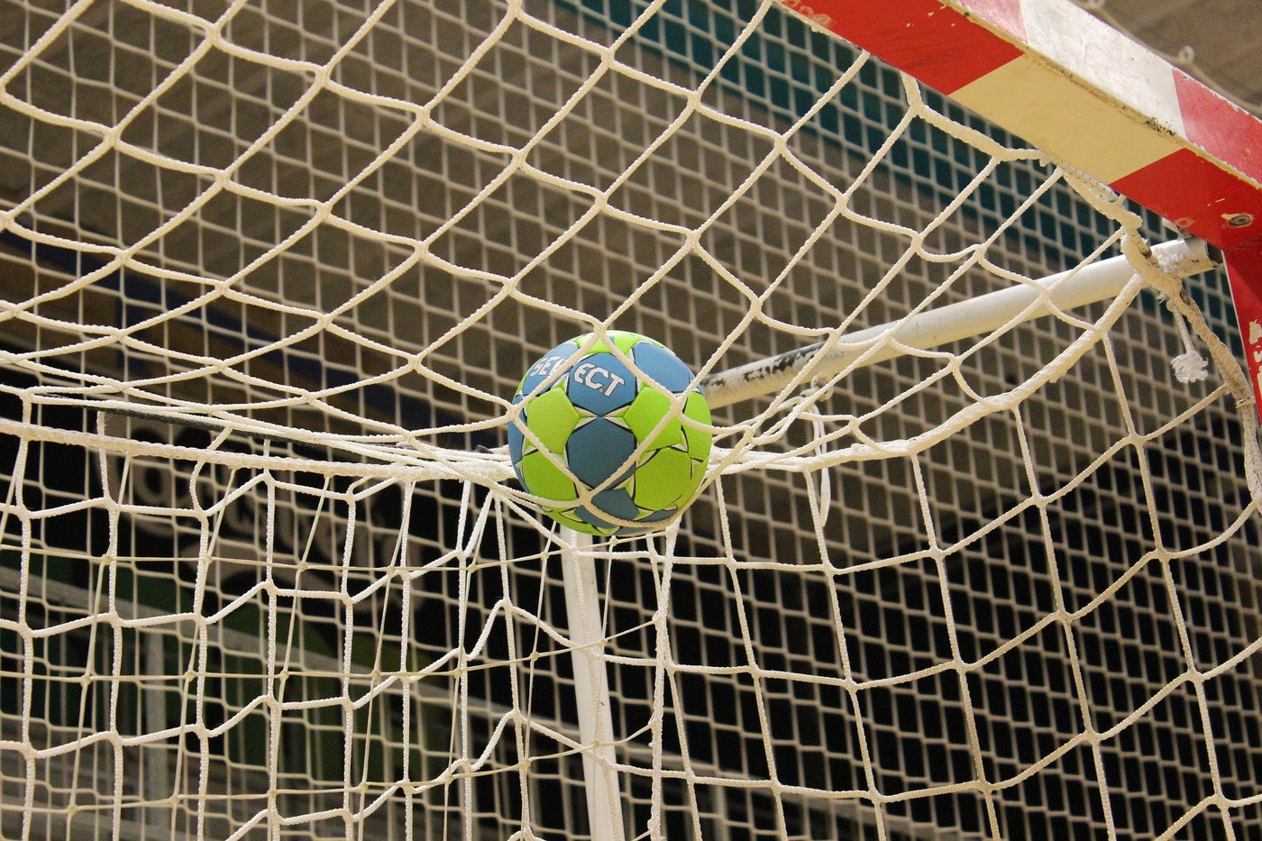 Ein grün-blauer Handball landet auf dem oberen Netz vom Tor - daneben! Damit gestresste Handballer und Handballerinnen immer die Möglichkeit haben zu erfrischen, sind unsere 720°DGREE-Trinkflaschen die perfekte Lösung.